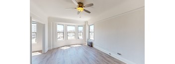 an empty living room with a ceiling fan and three windows