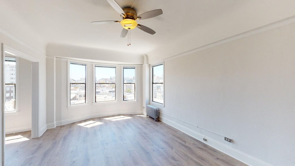 an empty living room with a ceiling fan and three windows