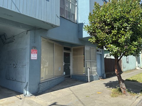 A tree is in front of a grey building with a sign on it.