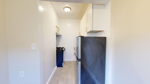 A kitchen with a refrigerator, trash can, and cabinets.