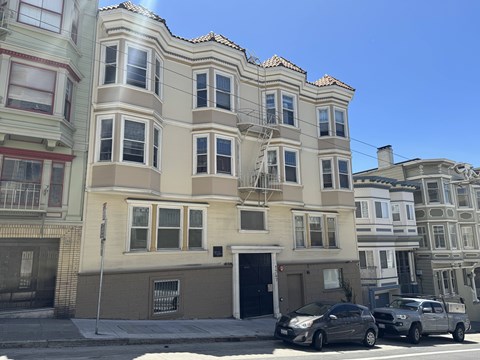 A row of multi-story buildings with cars parked in front.