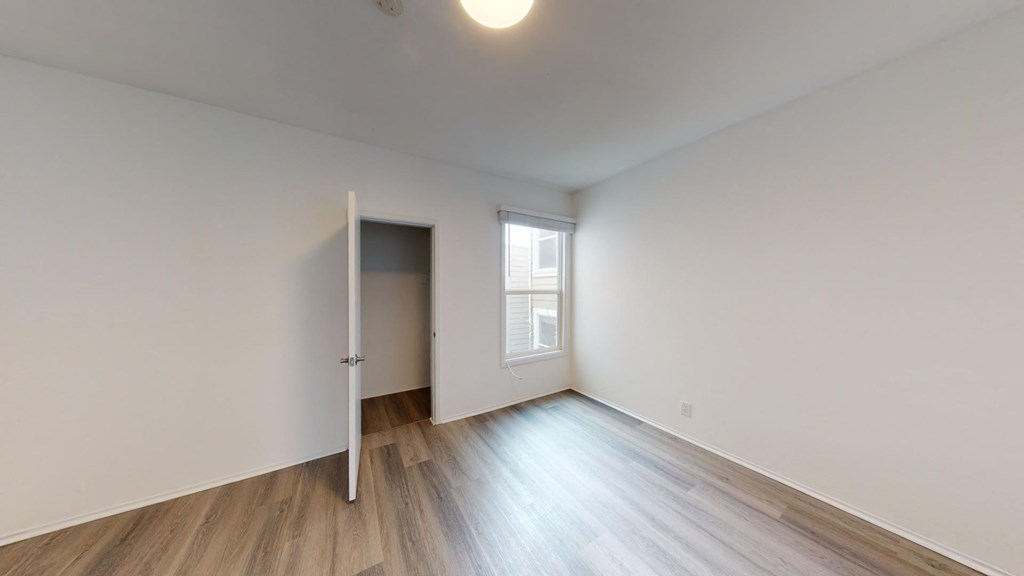a bedroom with white walls and wood flooring and a window