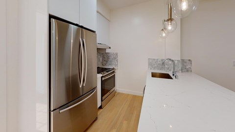 Sleek kitchen with stainless steel fridge, marble countertops, and modern pendant lights. Wooden floor and backsplash add elegance.
