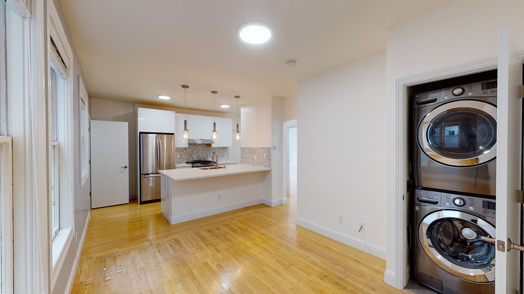 a living room with a washing machine and a kitchen with a sink