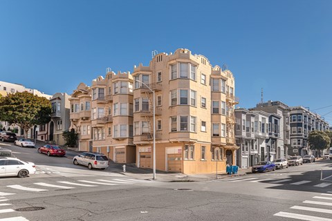 A street view of a residential building with cars parked on the side of the road.