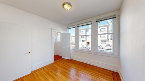 A room with a wooden floor and a window overlooking a cityscape.