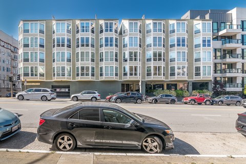A black car is parked on the side of a street in front of a multi-story building.