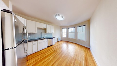 A kitchen with a refrigerator on the left and wooden floors.