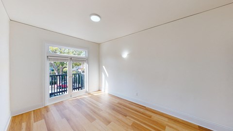 A room with wooden floors and a window with a view of trees and a fence.