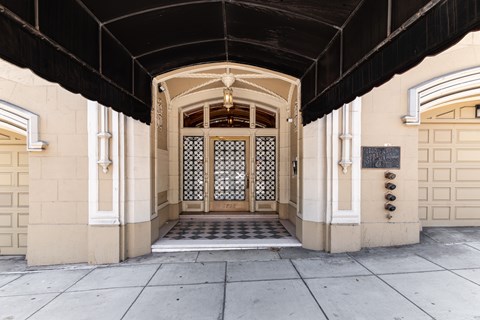 A large wooden door with a glass panel and a metal grill is flanked by two white columns.