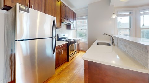 A kitchen with a stainless steel refrigerator and wooden cabinets.