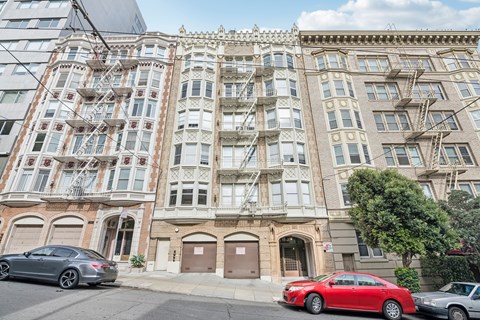 A red car is parked in front of a building with a fire escape.