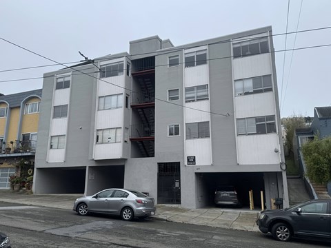A grey and white apartment building with cars parked in front.