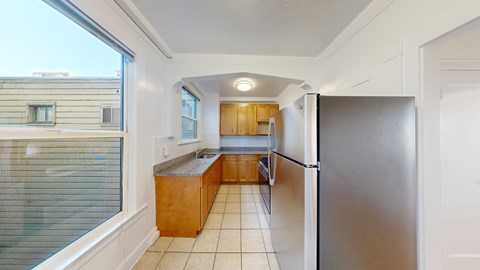 A kitchen with a refrigerator, sink, and wooden cabinets.