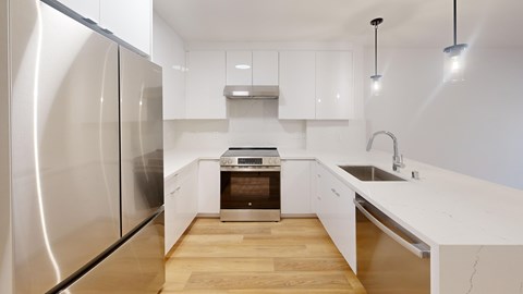 A modern kitchen with a stainless steel refrigerator and wooden flooring.