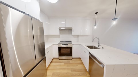 A modern kitchen with a stainless steel refrigerator and wooden flooring.