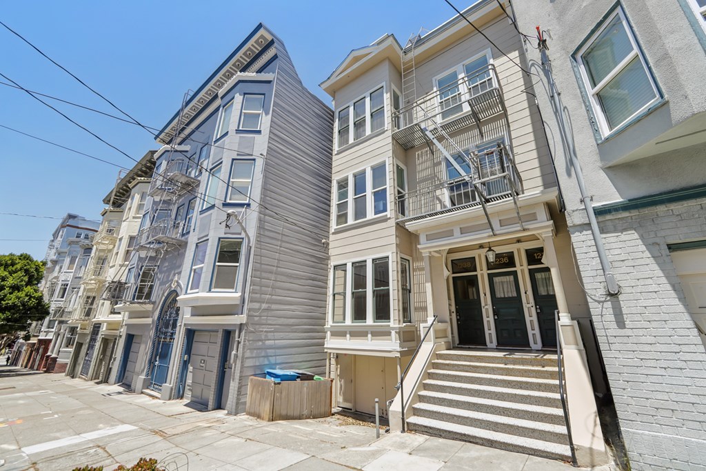 A row of three-story houses with white and grey facades and staircases leading to the doors.