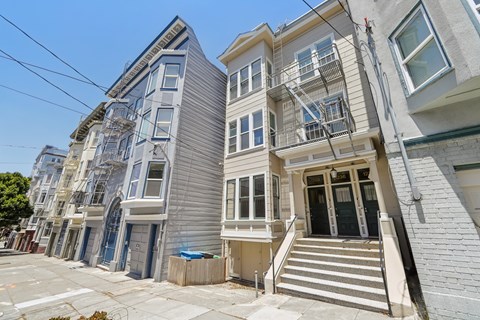 A row of three-story houses with white and grey facades and staircases leading to the doors.