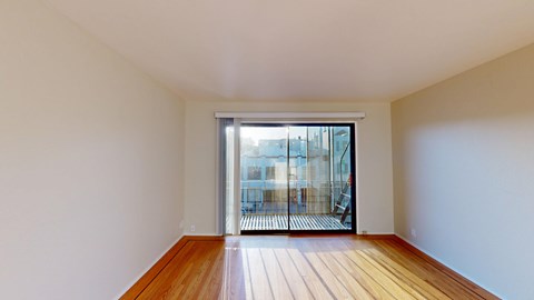 A room with wooden floors and white walls leading to a glass door.