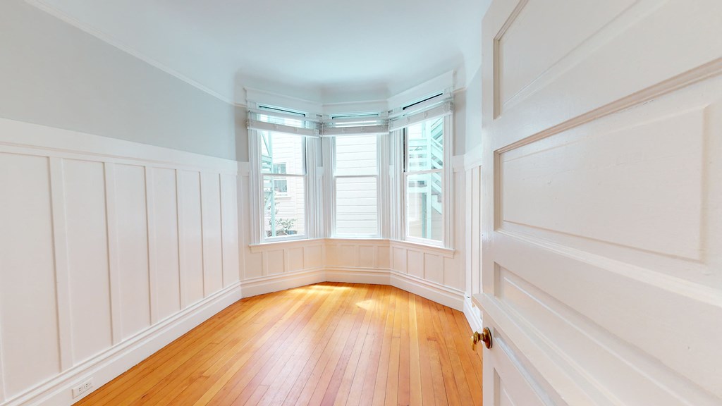 a living room with white walls and wood floors and a bay window