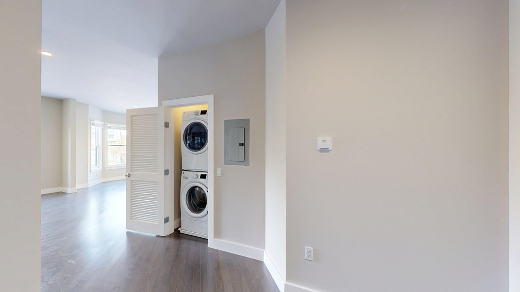 A white door opens to a room with a washer and dryer stacked on top of each other.