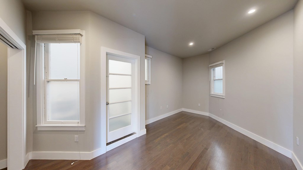 A room with wooden floors and three windows.