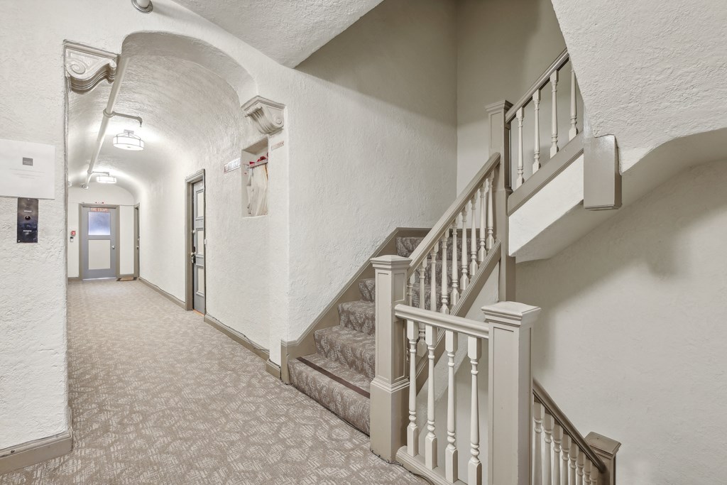 Hallway with a carpet, set of stairs with a railing and banister