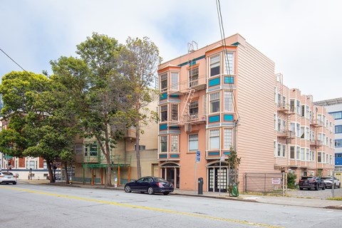 A street view of a multi-story building with cars parked in front.