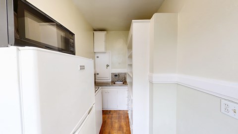 A white kitchen with a microwave on top of the fridge.