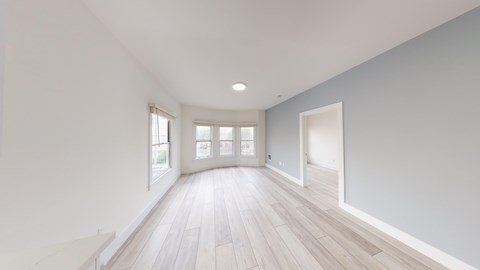 A spacious room with light wood flooring and white walls.