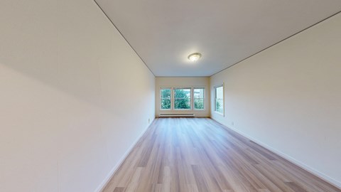 A long, empty room with wooden floors and a window at the end.