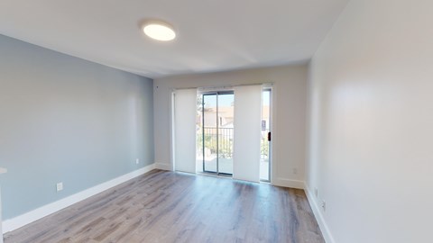 A spacious room with a sliding glass door leading to a balcony.
