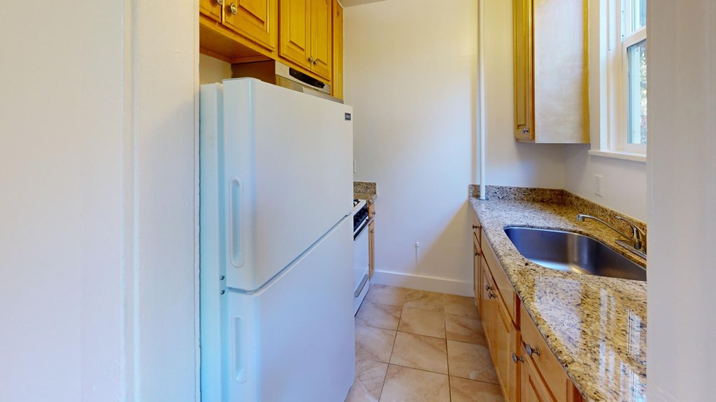 A white refrigerator stands in a kitchen with wooden cabinets and a granite countertop.