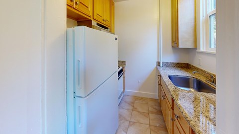 A white refrigerator stands in a kitchen with wooden cabinets and a granite countertop.