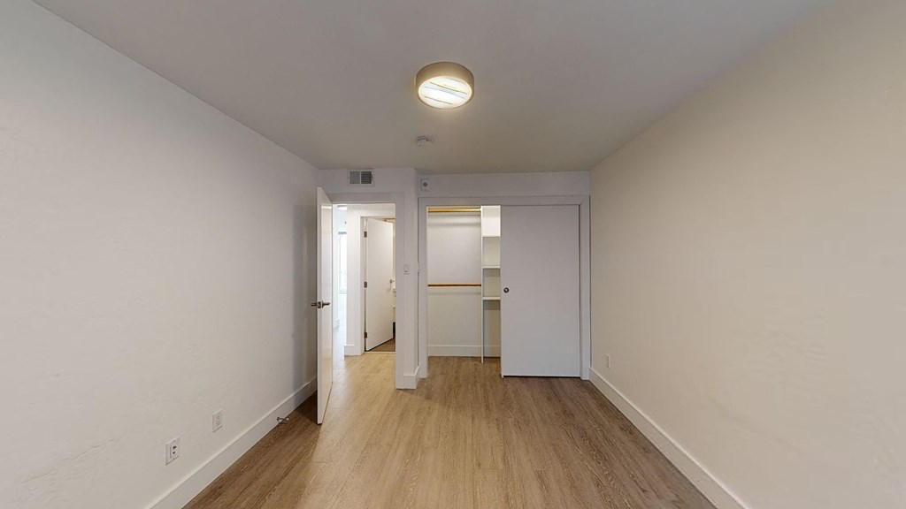 a bedroom with white walls and wood flooring and a closet