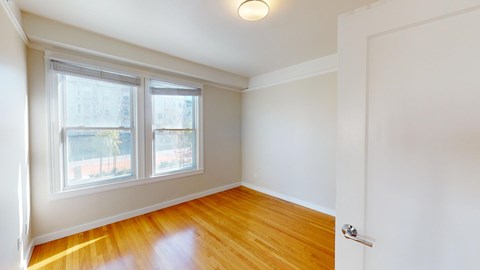A room with a wooden floor and a window overlooking a street.