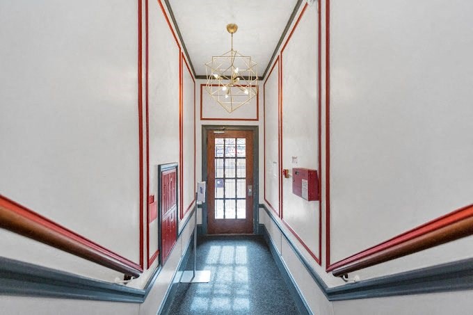 A hallway with a chandelier and a door at the end.