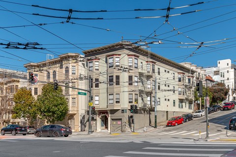 A street view of a city with cars, buildings, and a tram overhead.