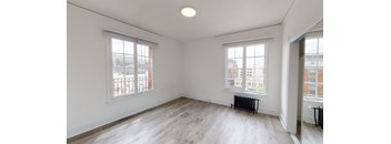 an empty living room with two windows and wood flooring
