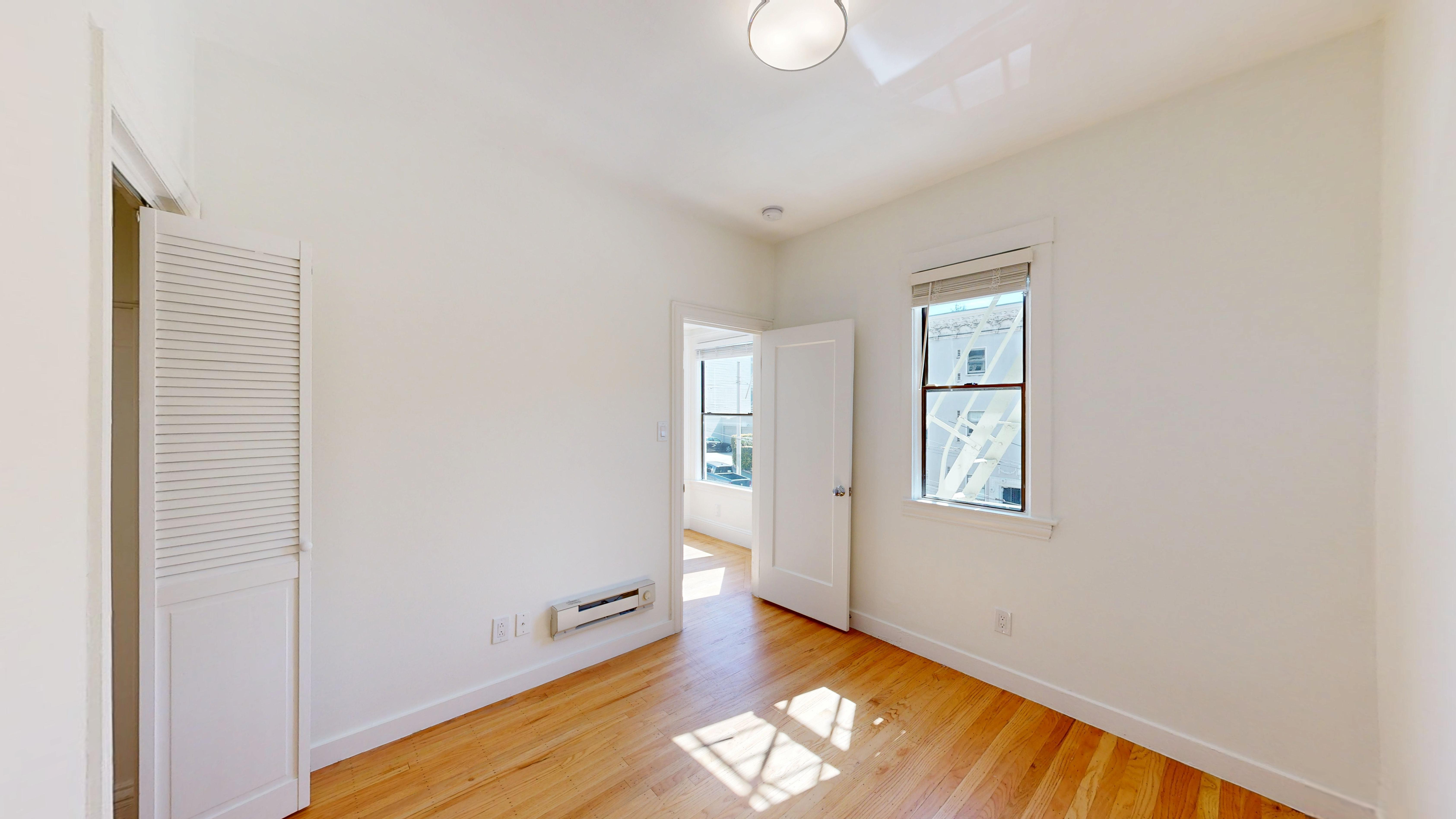 A room with a wooden floor and a window with blinds.