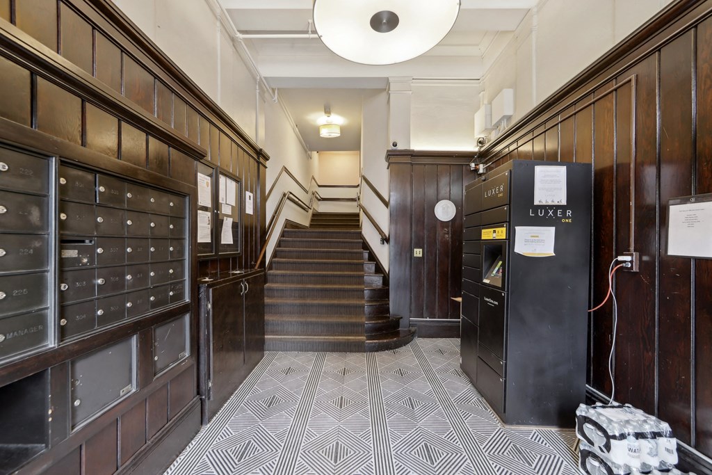 Entrance hall featuring wooden paneling, mailboxes, staircase, and a Luxer package locker against a patterned floor