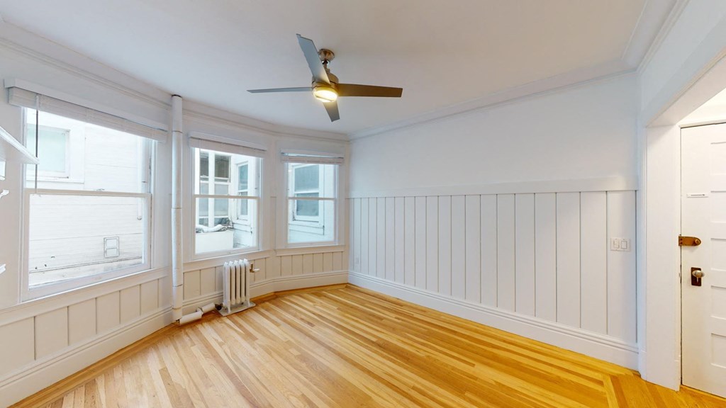 a living room with white walls and wood floors and a ceiling fan