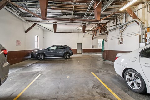 A grey car is parked in a garage with a white car on the right.