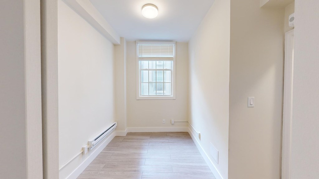 A long, narrow hallway with a window and wooden floors.