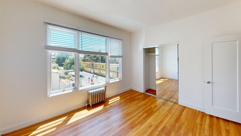 A room with wooden floors and a large window with blinds.