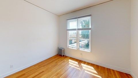 A room with wooden floors and a window showing a view of a building.