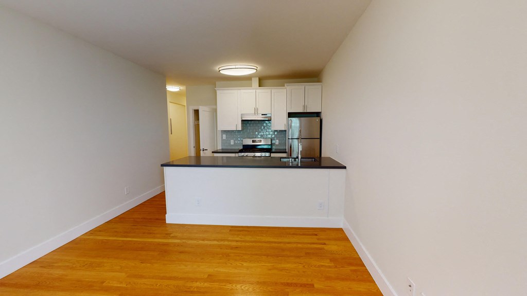 a view of a living room and kitchen with wood floors and white walls