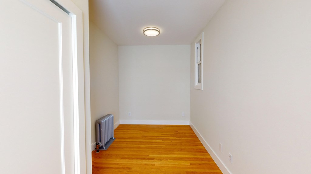 an empty room with a wood floor and white walls and a white radiator