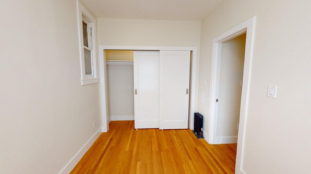 a bedroom with white walls and wood floors and a closet