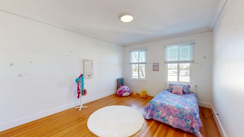 A room with a bed, a rug, a window, and a wall hanging.